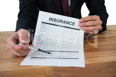 Mid section of businessman sitting at desk holding insurance contract