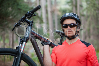 Portrait of male mountain biker carrying bicycle in the forest