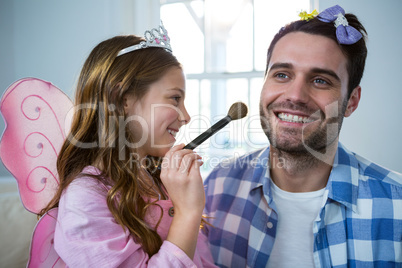 Girl dressed up in a fairy costume applying make-up on fathers face