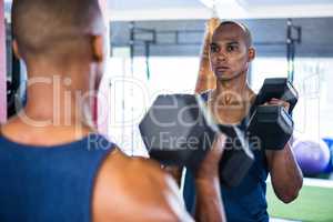 Reflection of male athlete exercising with dumbbell