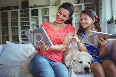 Smiling mother and daughter sitting with pet dog and using digital tablet