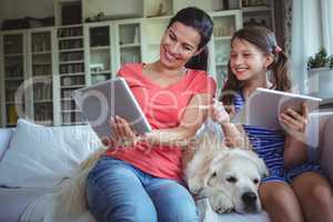 Smiling mother and daughter sitting with pet dog and using digital tablet