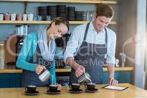 Waiter and waitress making cup of coffee at counter in cafe