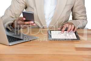 Mid-section of Businesswoman using mobile phone and digital tablet with laptop on table