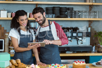 Smiling waiter and waitress using digital tablet at counter