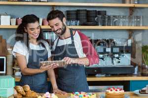 Smiling waiter and waitress using digital tablet at counter