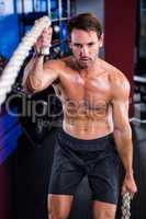 Shirtless man holding rope in gym