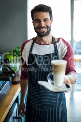 Smiling waiter holding cup of cold coffee at counter in cafe