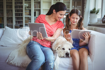 Mother and daughter sitting with pet dog and using digital