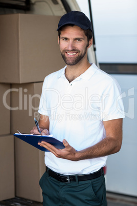 Delivery man writing on clipboard while standing next to his van