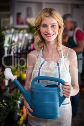 Smiling female florist holding watering can in flower shop