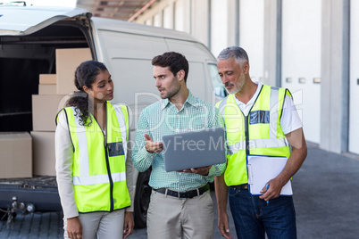Manager and warehouse workers discussing with laptop