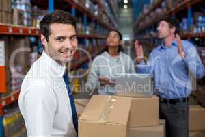 Warehouse manager carrying a box and his colleagues discussing
