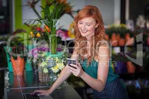 Female florist using mobile phone while using laptop