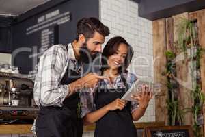 Smiling waiter and waitress interacting while using digital tablet