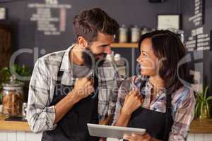 Smiling waiter and waitress interacting while using digital tablet