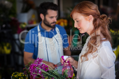 Woman spraying water on bunch of flowers while man preparing flower bouquet