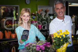 Smiling florist showing credit card terminal in flower shop
