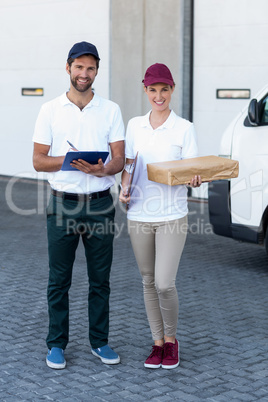 Portrait of delivery man and woman standing with clipboard and parcel