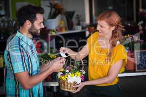 Female florist giving visiting card and flower basket to customer
