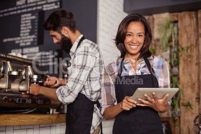 Waitress using digital tablet while waiter preparing coffee in background