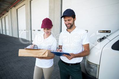 Happy delivery man and woman writing on clipboard next to van