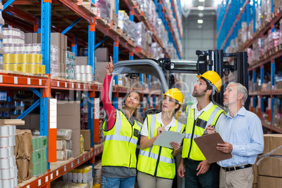 Warehouse manager and co-workers discussing over clipboard