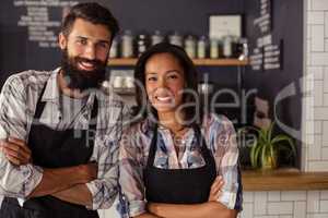 Portrait of smiling waiter and waitress standing with arms crossed