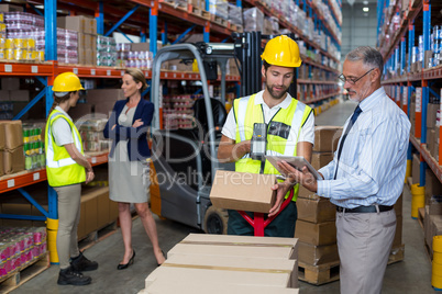 Warehouse manager holding digital tablet while male worker scanning barcode