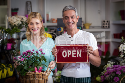 Florists holding open sign placard and flower basket in flower shop