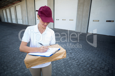 Smiling delivery woman writing on clipboard