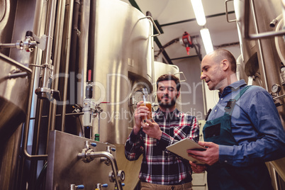 Owner inspecting beer with worker at brewery