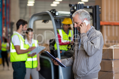 Warehouse manager talking on mobile phone and holding a clipboard