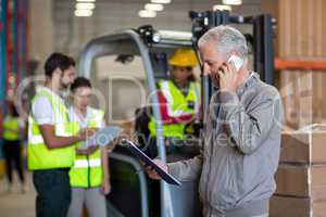 Warehouse manager talking on mobile phone and holding a clipboard
