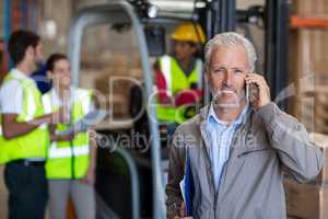 Warehouse manager talking on mobile phone and holding a clipboard