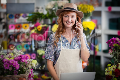 Female florist talking on mobile phone while using laptop