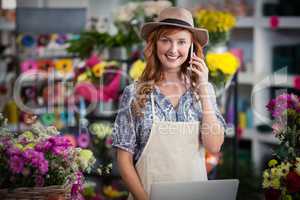 Female florist talking on mobile phone while using laptop