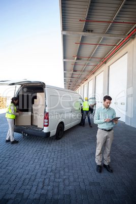 Manager working on tablet and warehouse workers loading the cardboard boxes