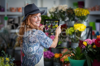 Female florist taking photograph of flowers from digital tablet in flower shop