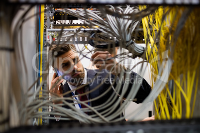 Technician talking on mobile phone while checking cables