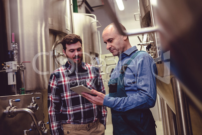 Worker and owner discussing over digital tablet at brewery