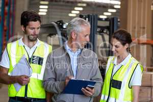 Warehouse manager and workers discussing with clipboard