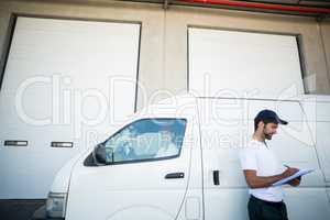 Delivery man writing on clipboard while standing next to his van