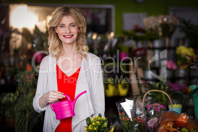 Happy female florist holding a watering can in flower shop