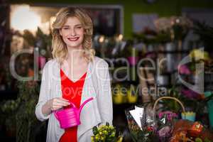 Happy female florist holding a watering can in flower shop