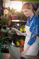 Female florist using laptop while holding clipboard