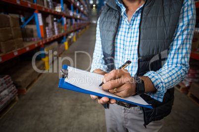 Mid section of warehouse worker writing on clipboard