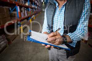 Mid section of warehouse worker writing on clipboard