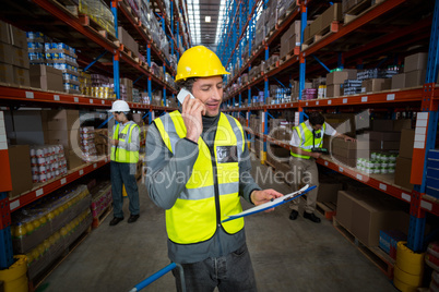 Warehouse worker talking on mobile phone and holding clipboard