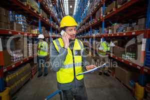 Warehouse worker talking on mobile phone and holding clipboard